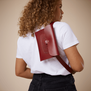 A woman with curly blonde hair wearing a white t-shirt and a red crossbody leather bag.