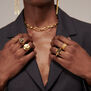 A model with dark skin wearing a grey blazer and several gold rings. The photo shows a close up to her hands and chest.