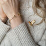 A woman wears a bracelet and a brooch featuring red-breasted flying robins. The photo shows a close up of her wrist and shoulder.