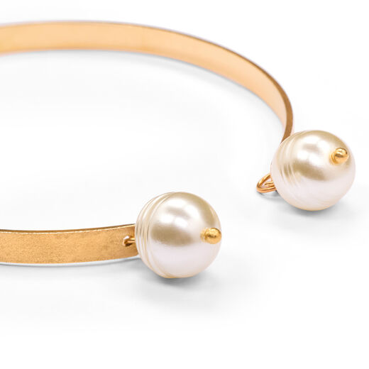 Detail of a gold bracelet featuring two white faux pearls pendants.