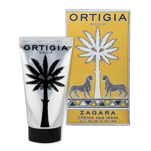 A silver hand cream bottle with a black cap. Next to it a paper box decorated with gold and silver tropical accents.