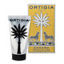 A silver hand cream bottle with a black cap. Next to it a paper box decorated with gold and silver tropical accents.