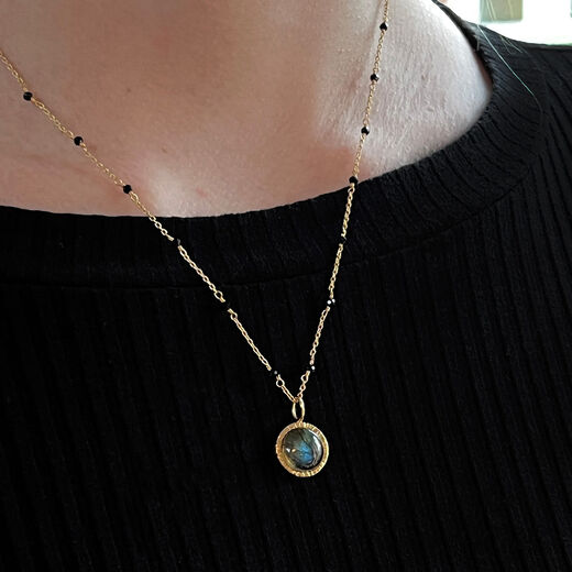 Close up of a white woman's neck, wearing a chain necklace on a black top.