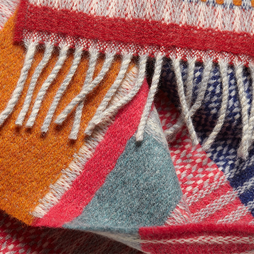 A detail of a wool scarf featuring a multicoloured pattern in pink and orange tones.