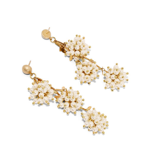 Two gold earrings with clusters of white faux pearls are photographed on a white tabletop.