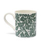 A white china mug with a pattern featuring a green pattern of oak leaves.
