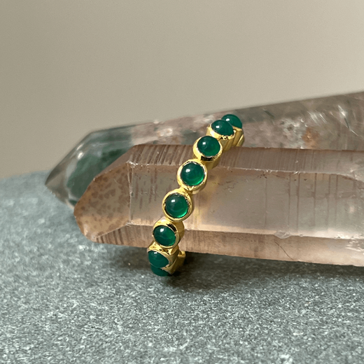 A gold ring with green onyx round stones photographed on a pink crystal. 