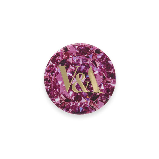 Round pin badge featuring a pink glitter pattern and the V&A logo in gold characters.
