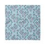 A pale blue square scarf featuring a pattern with pink flowers and red bows on a pale blue background.