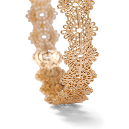 The detail of a gold cuff bracelet decorated with an ornate filigree pattern.