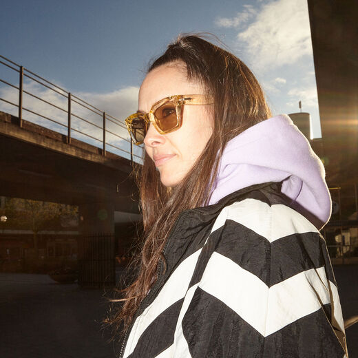 A young woman with long brown hair wearing a pair of sunglasses outdoors.