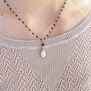 A white woman wearing a gold chain necklace with a pearl pendant and a cream jumper. The photo shows a detail of the neck.