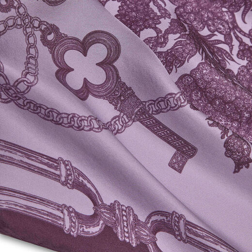 Close up of a pink and purple scarf with a print featuring an ornate key and details of jewellery.