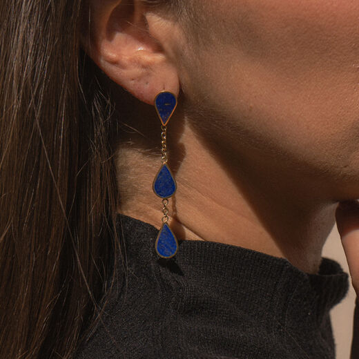 A close up of the neck and ear of a woman wearing a drop earring featuring three teardrop shaped lapis lazuli stones each.