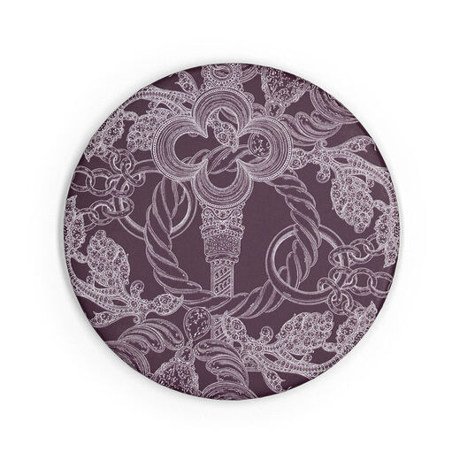 The back of a round purple pocket mirror. It features a detail of an intricate illustration of an old key.