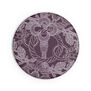 The back of a round purple pocket mirror. It features a detail of an intricate illustration of an old key.