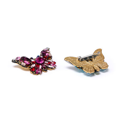 Two butterfly-shaped brooches. One is made of red gleaming stones and glass beads while the other is turned to show the clasp at its back.