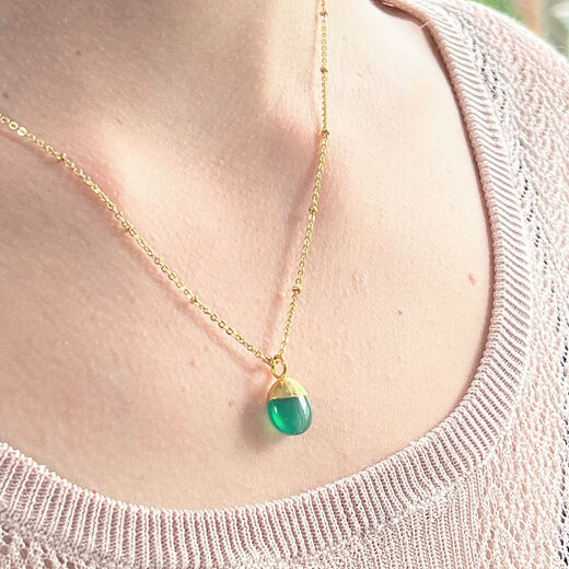 Close up of a white woman's neck wearing a gold chain necklace with a green pendant.