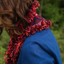 A woman with brown hair wears a blue jacket and a pink and purple woollen scarf.