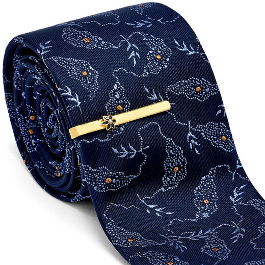 A silk tie featuring a delicate botanical pattern on navy fabric and a gold tie pin featuring an enamel flower in a matching colour.