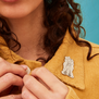Model wears three graces pin badge as an accent on the lapel of a colourful shirt