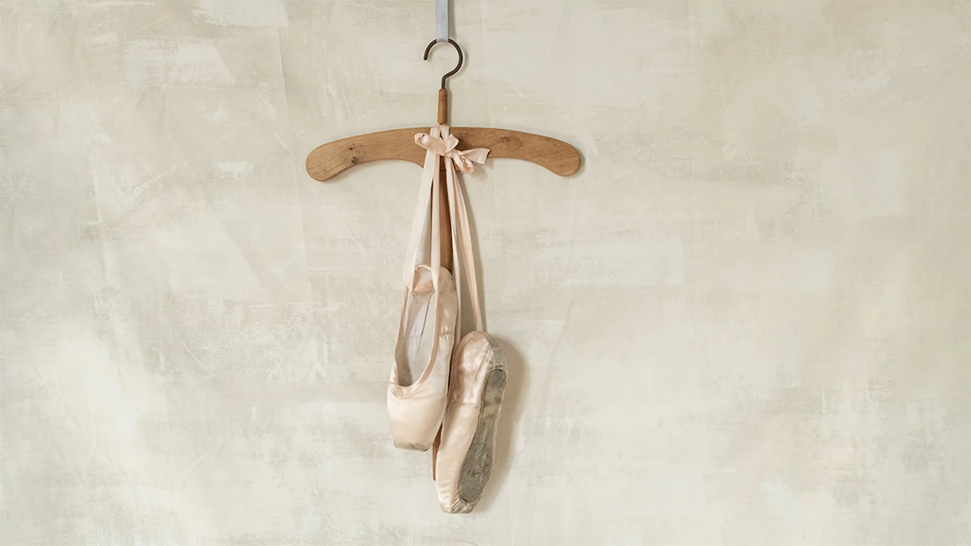 Pink ballet shoes hanging from a wooden hanger