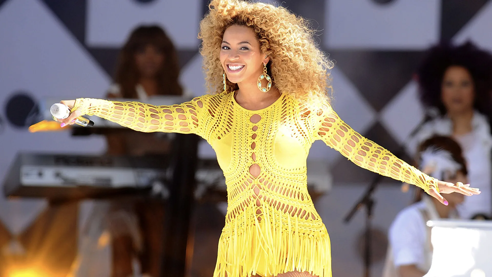 Beyoncé wearing a yellow dress on stage with her microphone in her hand