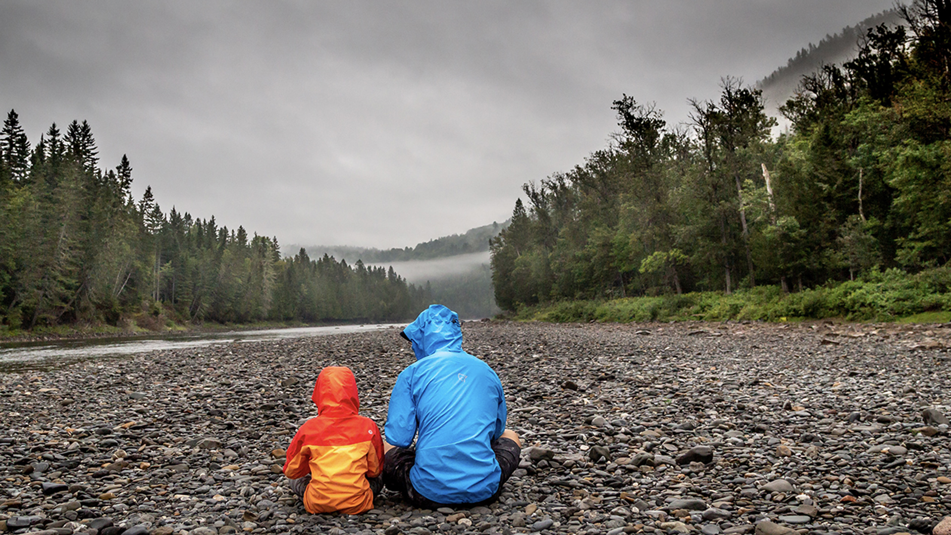 Man and boy in raincoats beside a river