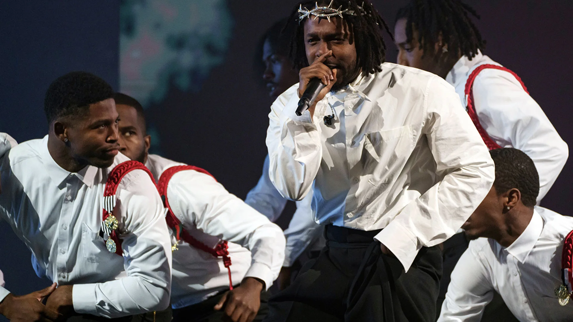 Kendrick Lamar rapping with a crown of thorns, and dancers surround him in white shirts