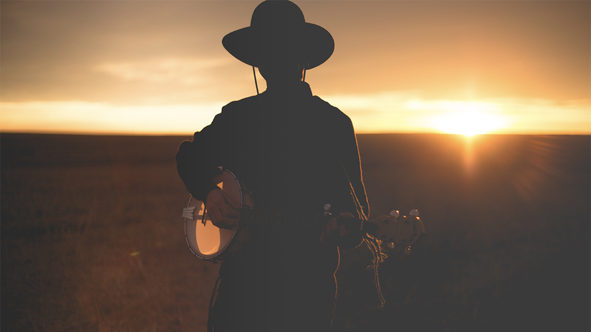 Man wearing a cowboy hat playing the guitar at sunset