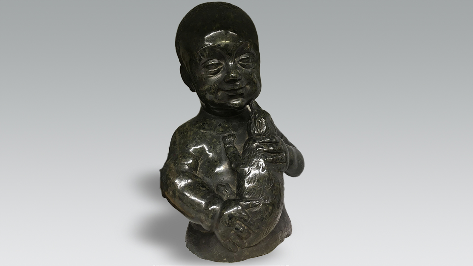 Dark green sculpture of a boy holding an animal