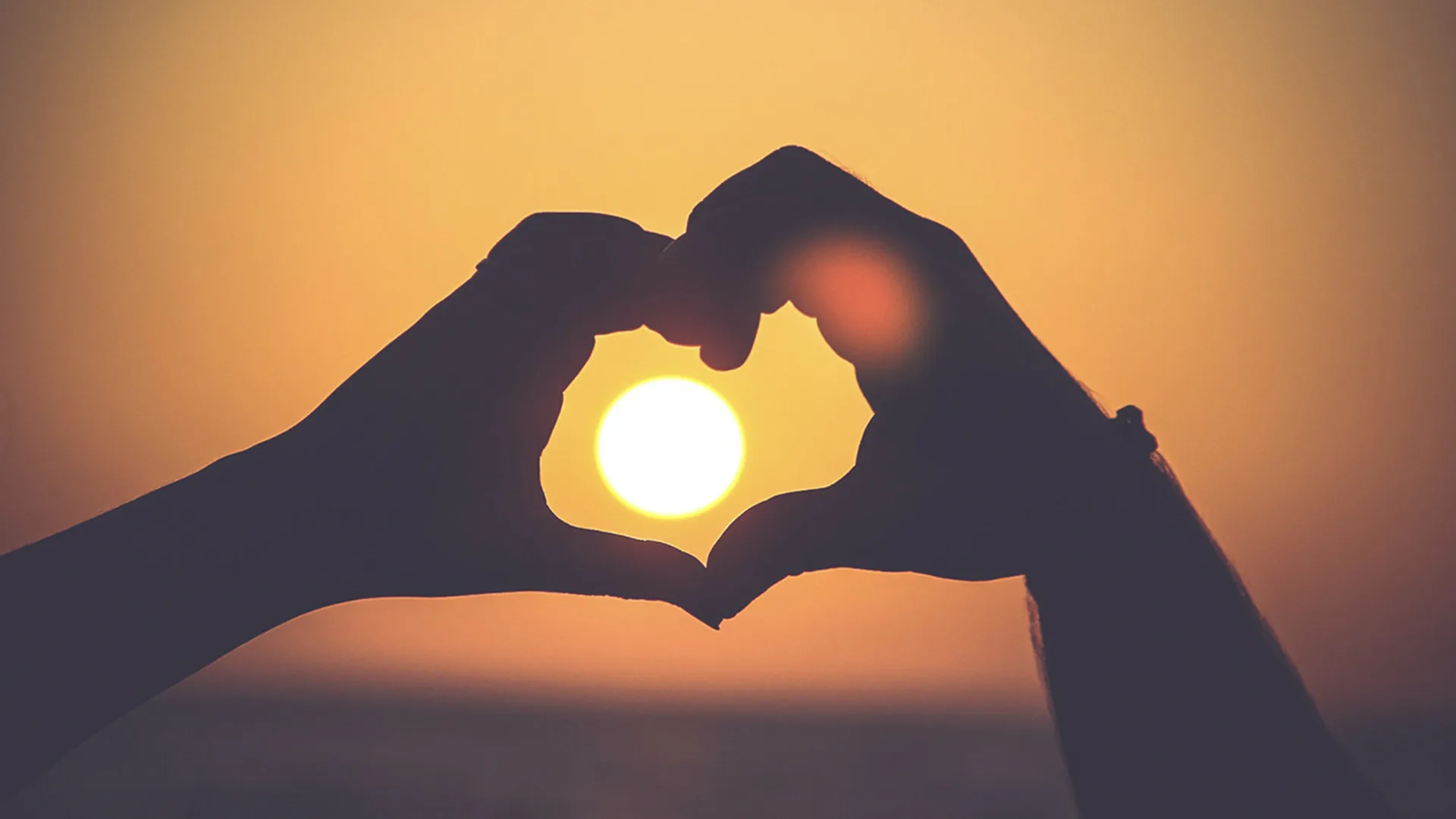 Silhouette of two peoples hands forming heart at sunset