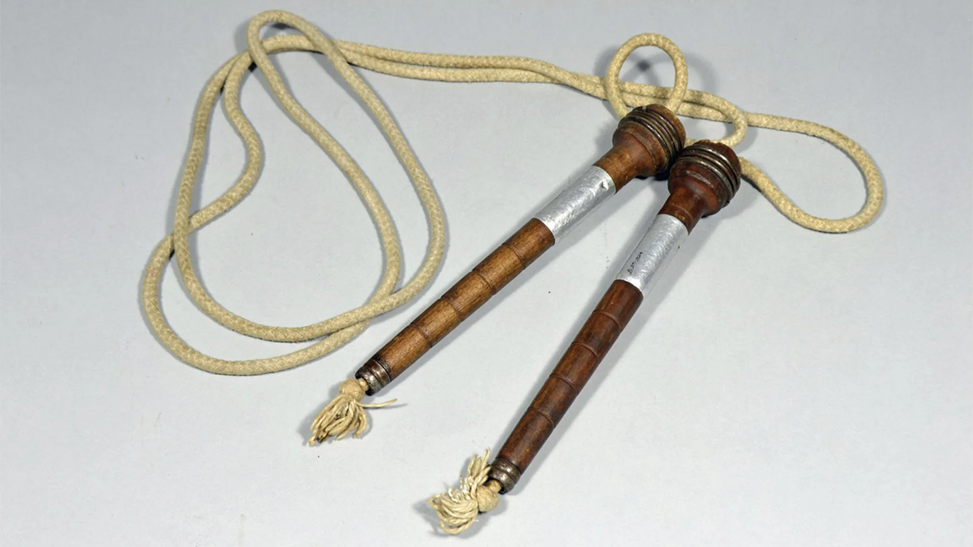 Old skipping rope with wooden handles on white surface. 