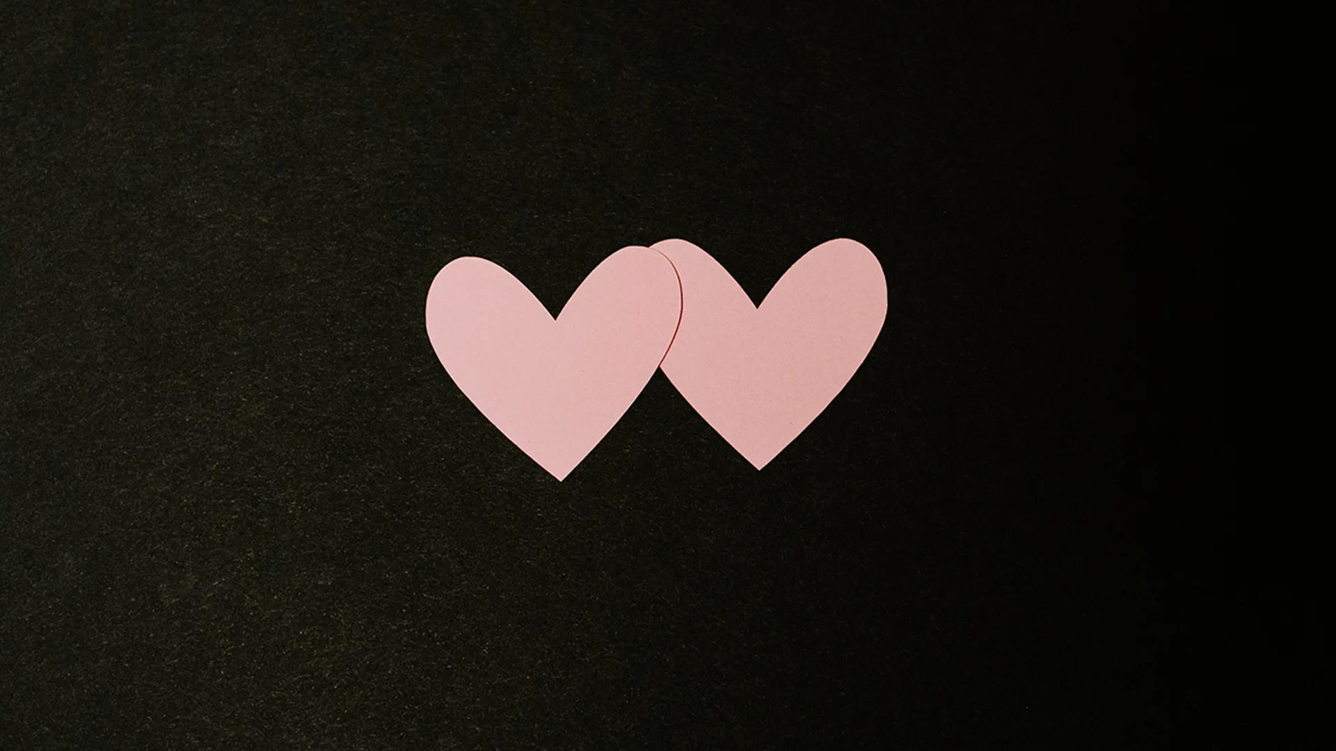 Two pink paper heart cutouts on a black background