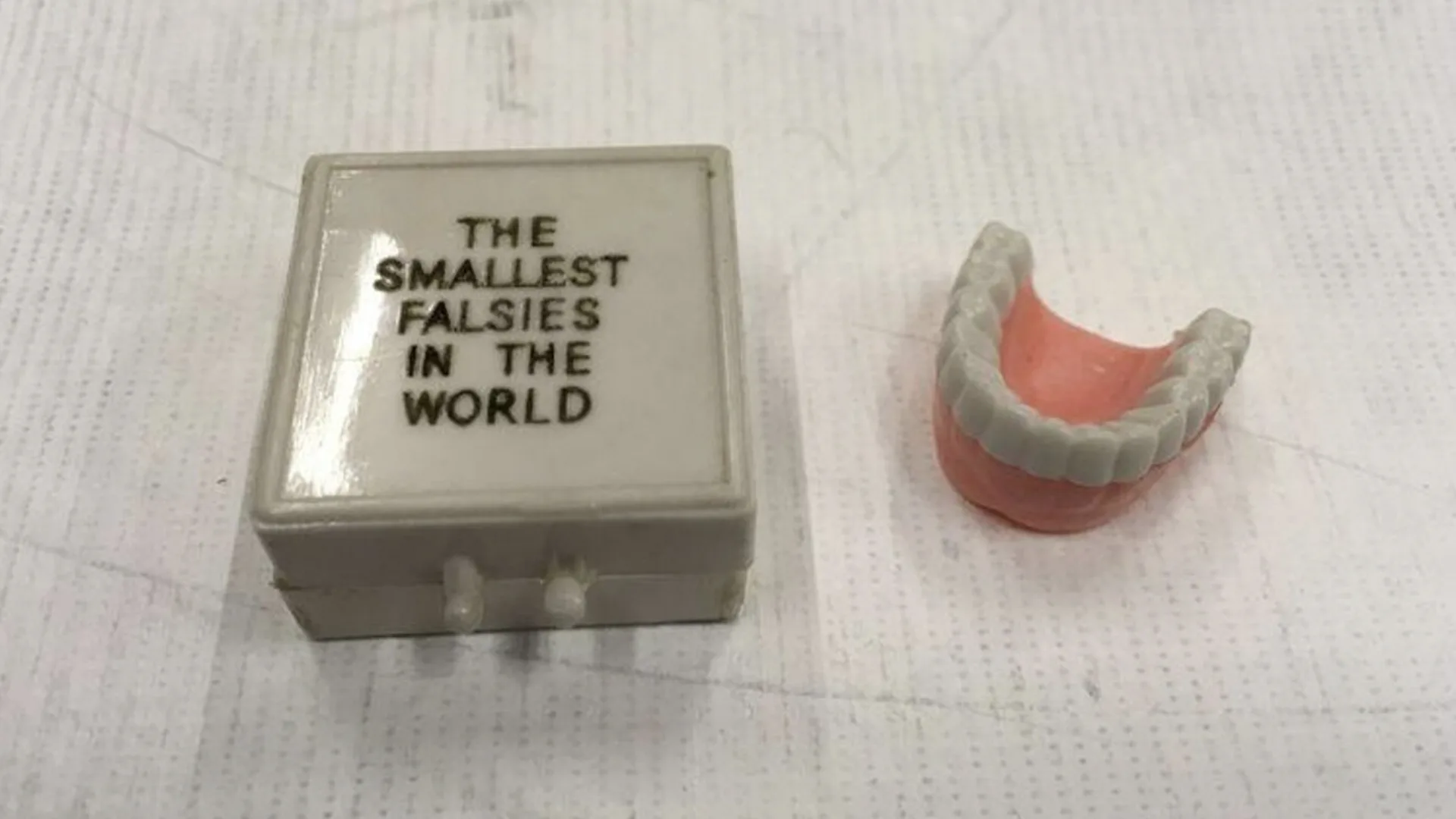 Fake teeth next to a white box which say 'The smallest falsies in the world' in capital letters