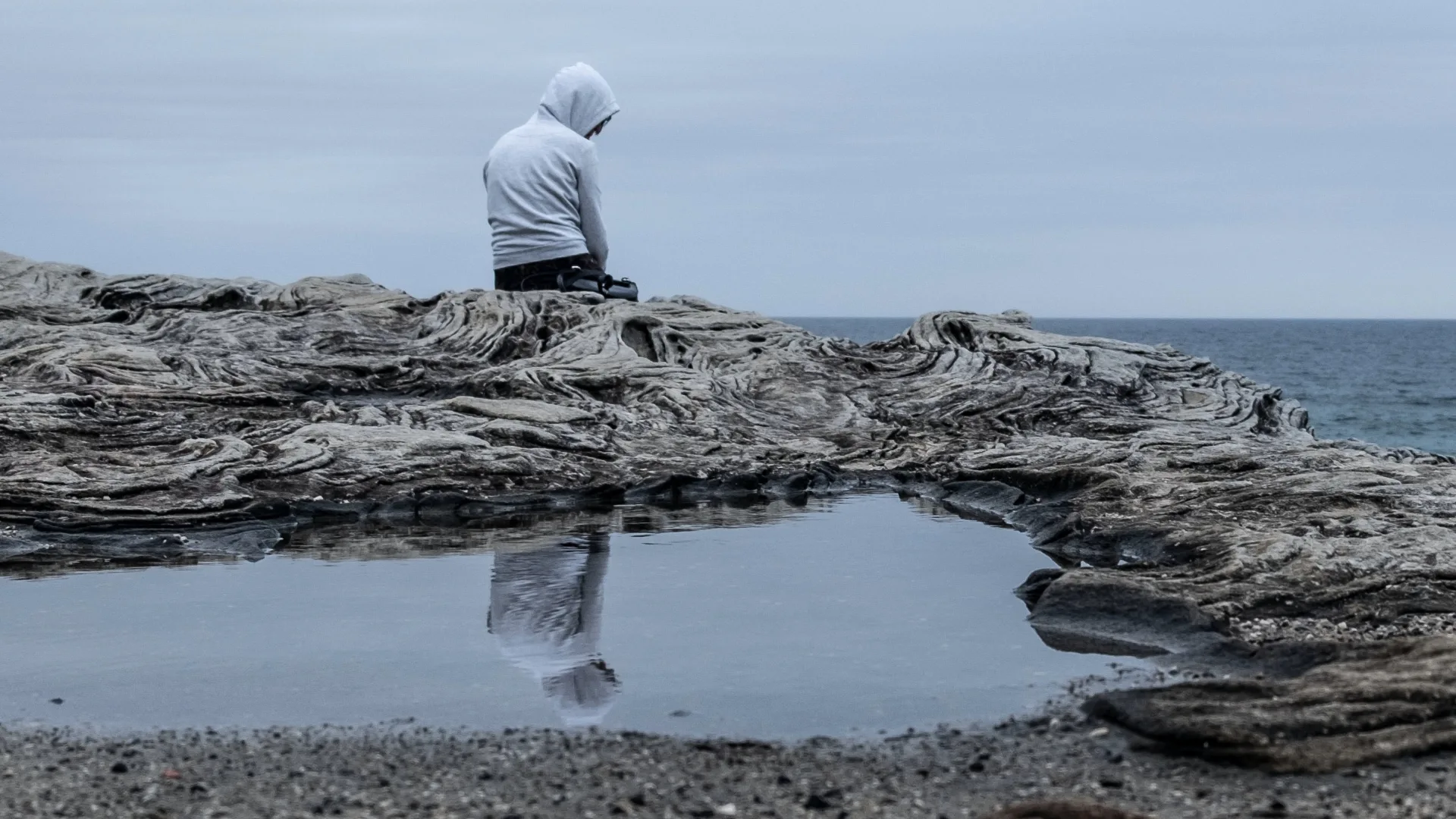 Person wearing a hoody sitting on a cliff looking out to sea