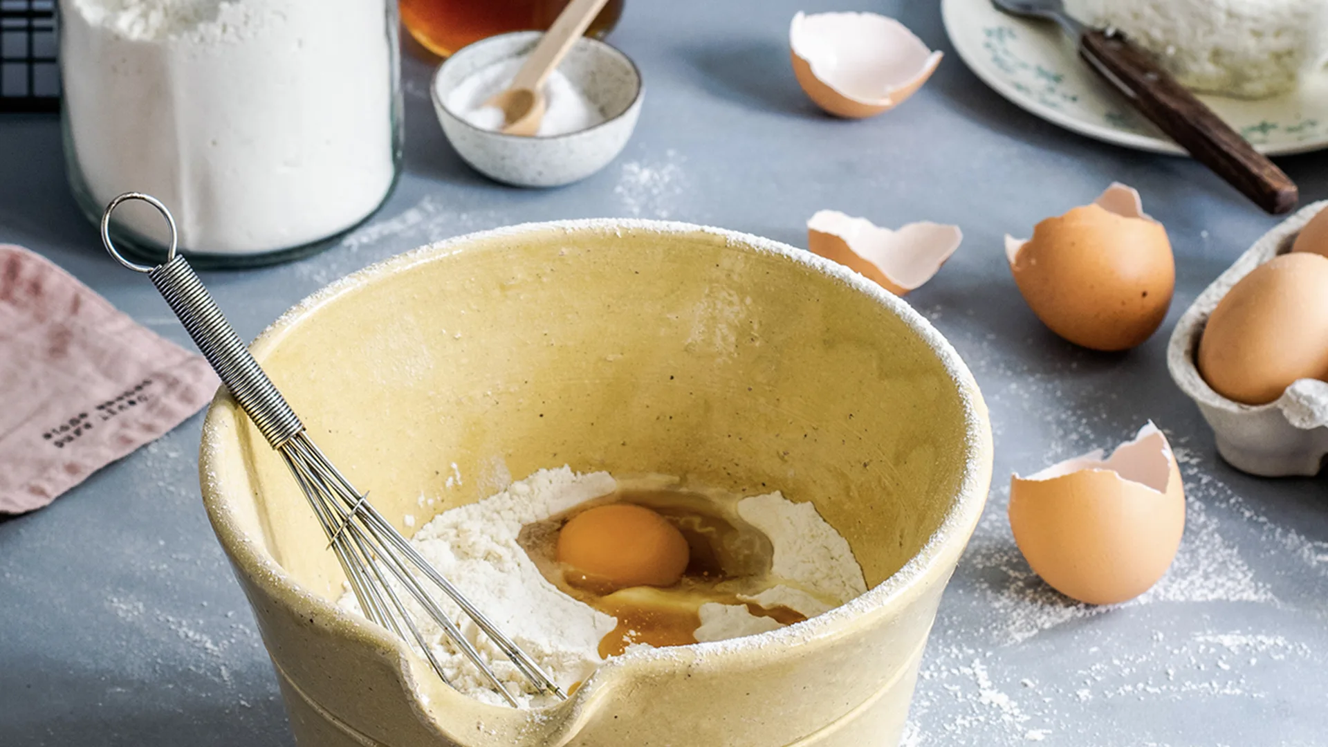 Bowl with ingredients in it, flour and eggshells to the side of it