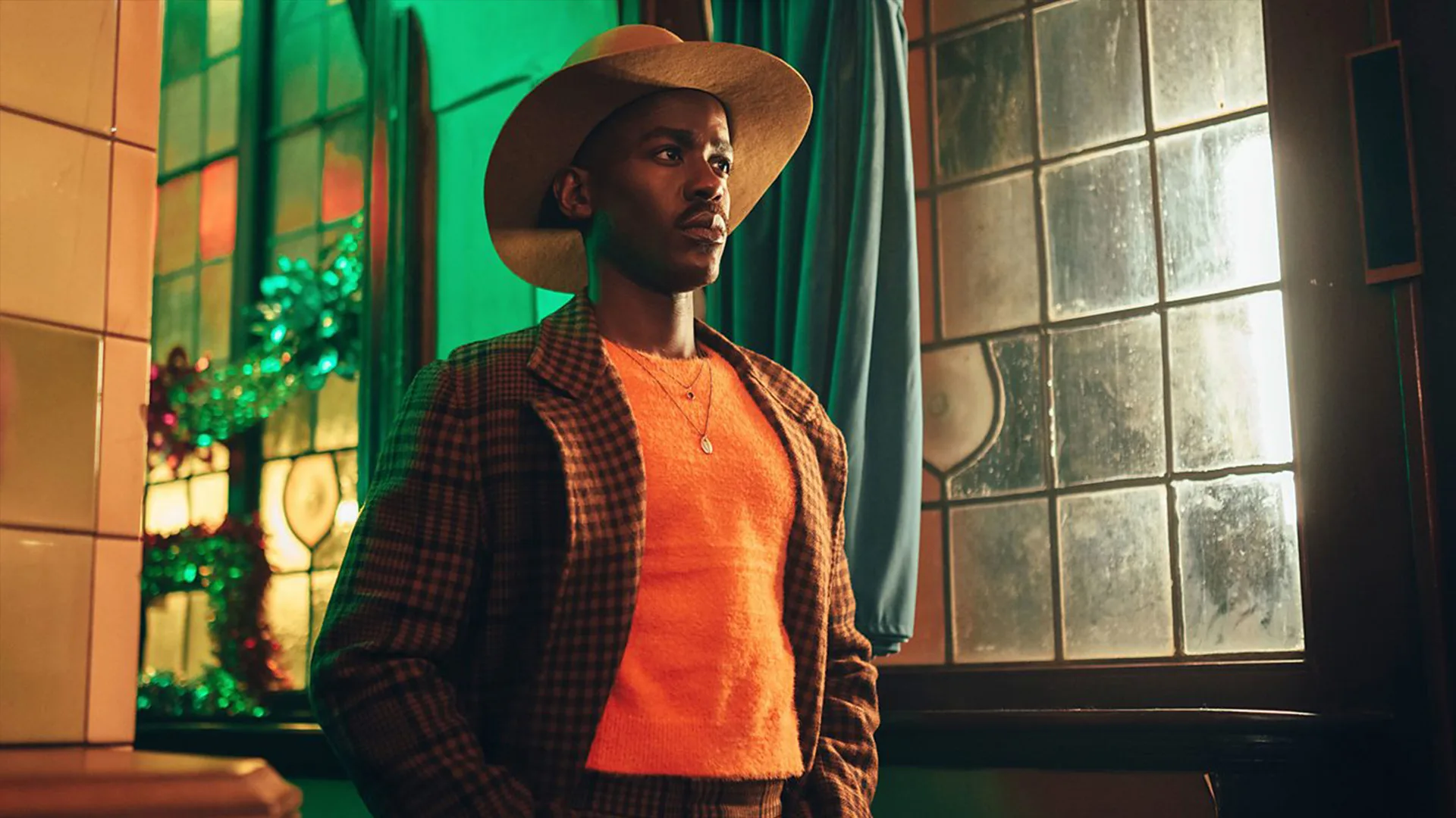 Actor Ncuti Gatwa in orange top and cowboy hat against green background
