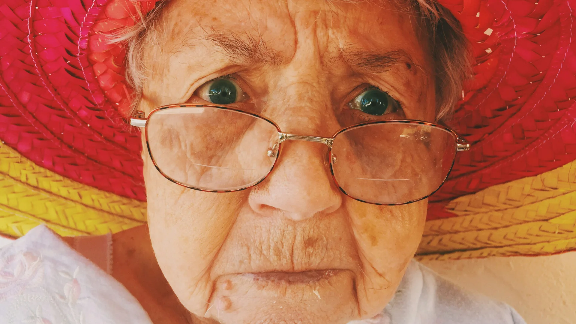 An old woman with glasses and hat looking directly at the camera, very sternly