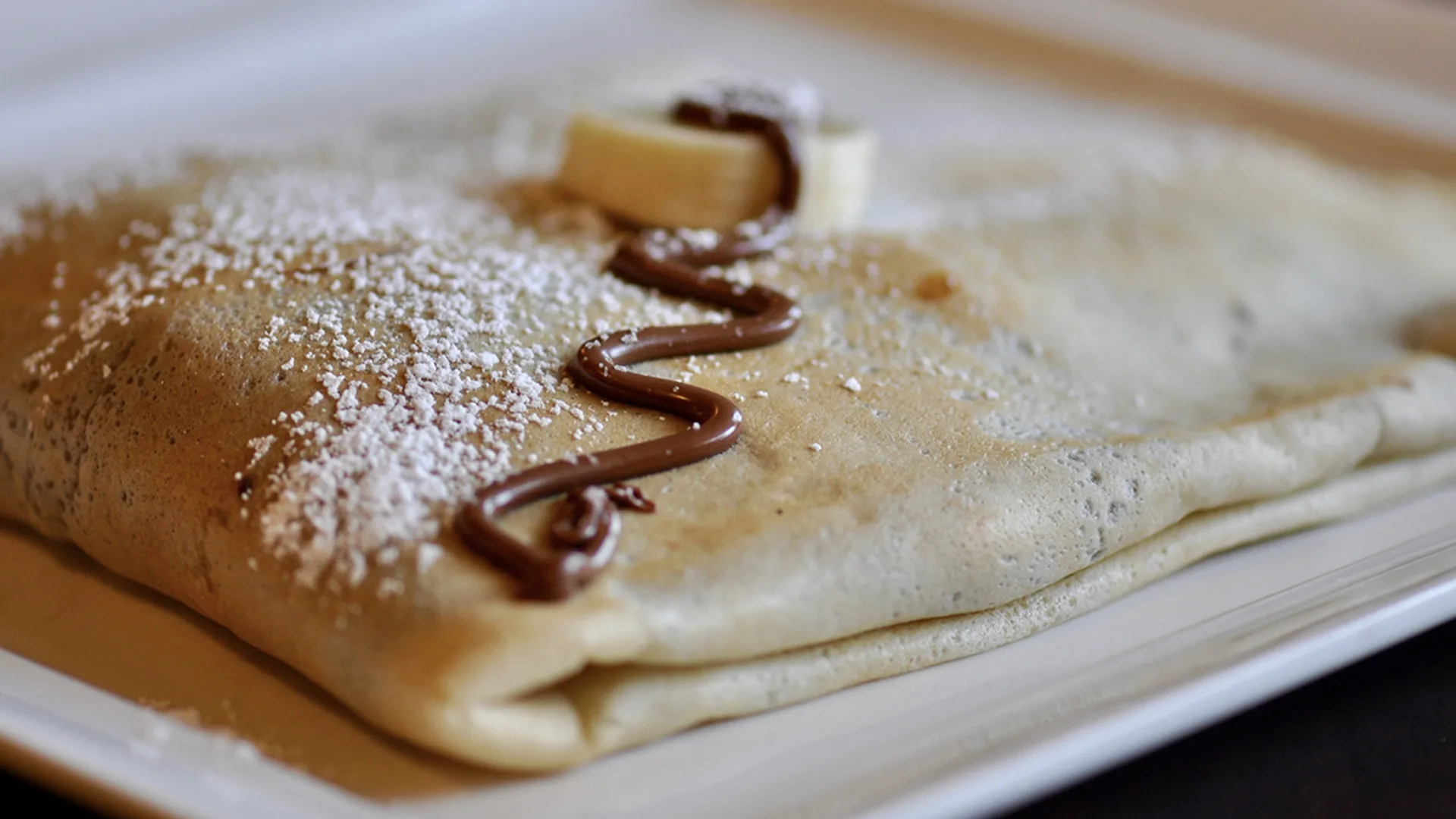 Close up of a crepe with icing sugar and chocolate