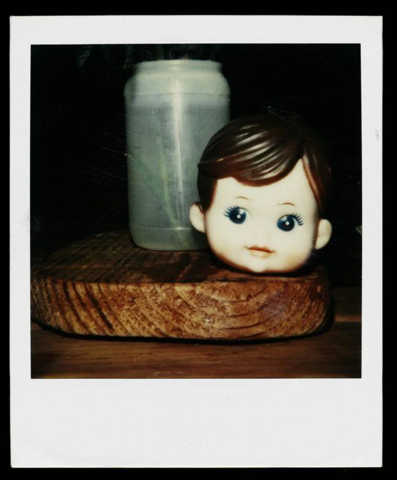 Polaroid photo depicting a dolls head next to a plastic container