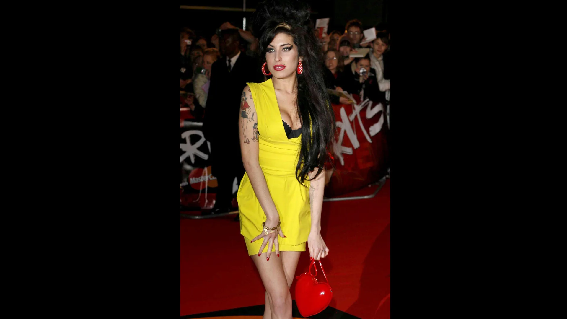 Photograph of Amy Winehouse wearing a yellow dress on the red carpet of the Brit Awards 2007