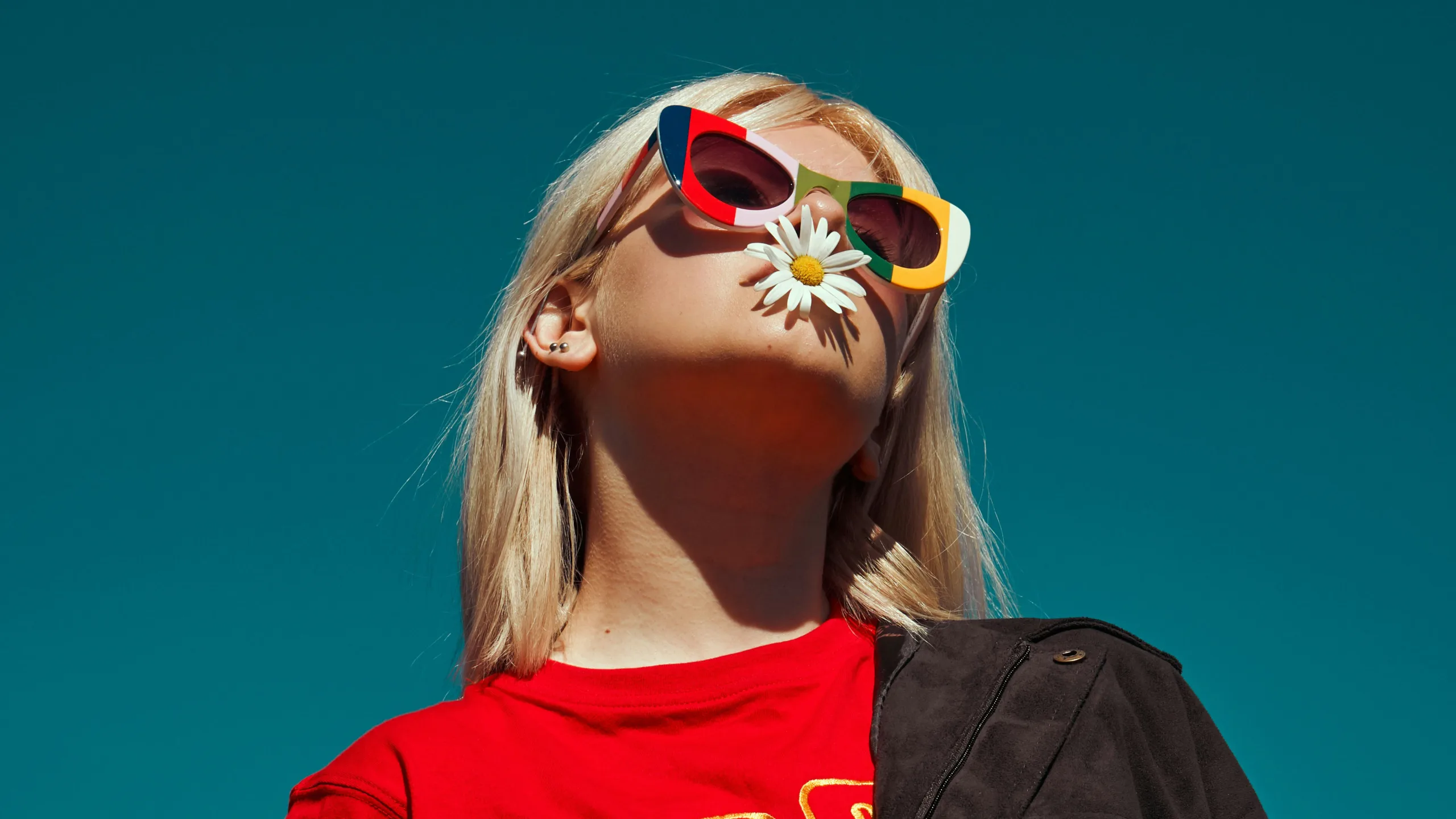 A photograph of a woman wearing sunglasses with a flower in her mouth