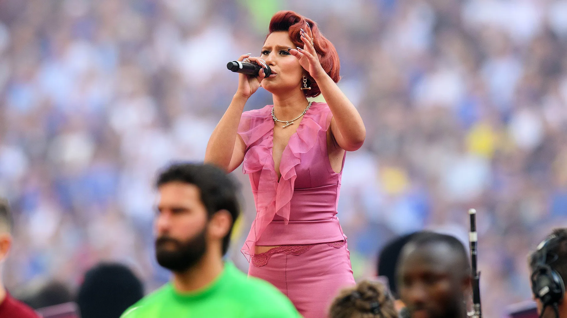 A photograph of Raye wearing a pink outfit singing to a crowd at a festival