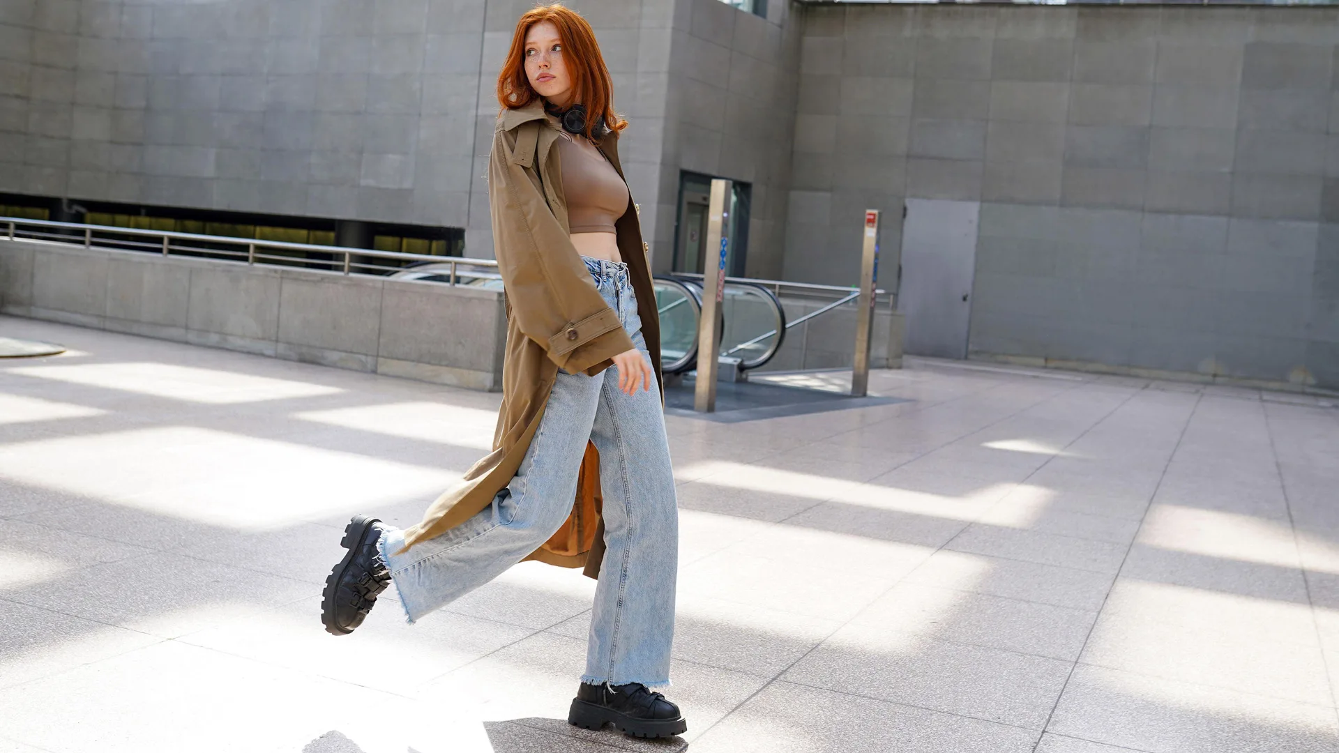 Ginger haired woman in blue jeans and trench coat walking down the street 