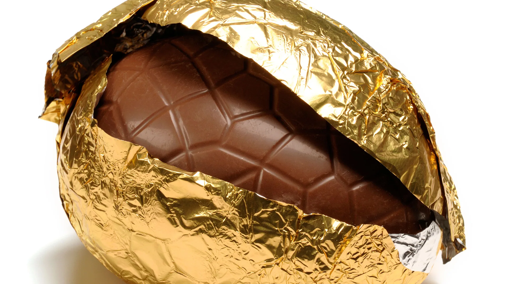 A close-up photograph of a chocolate easter egg in gold foil partially unwrapped exposing some of the chocolate against a white background