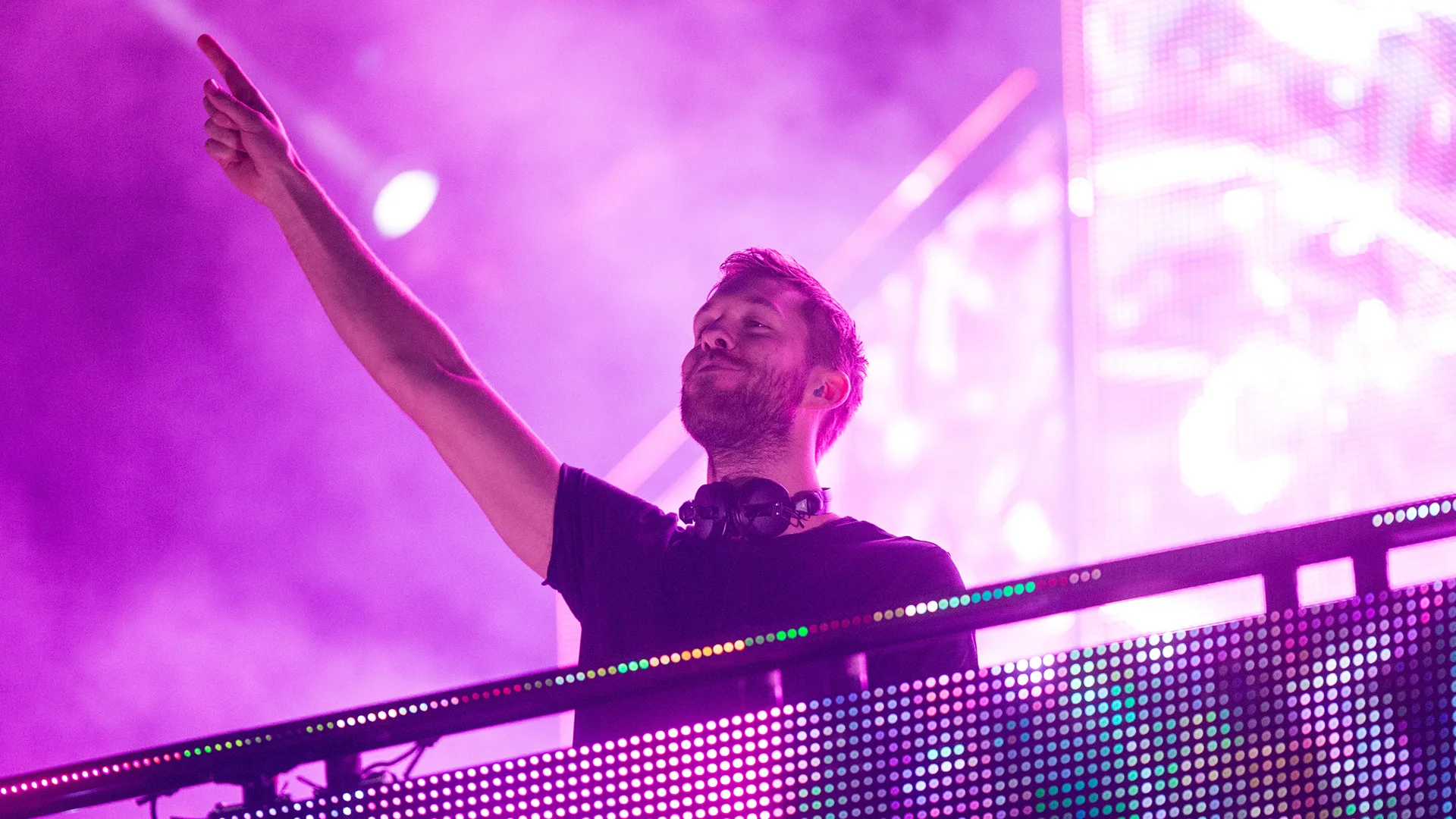 Calvin Harris standing behind DJ booth against a purple background