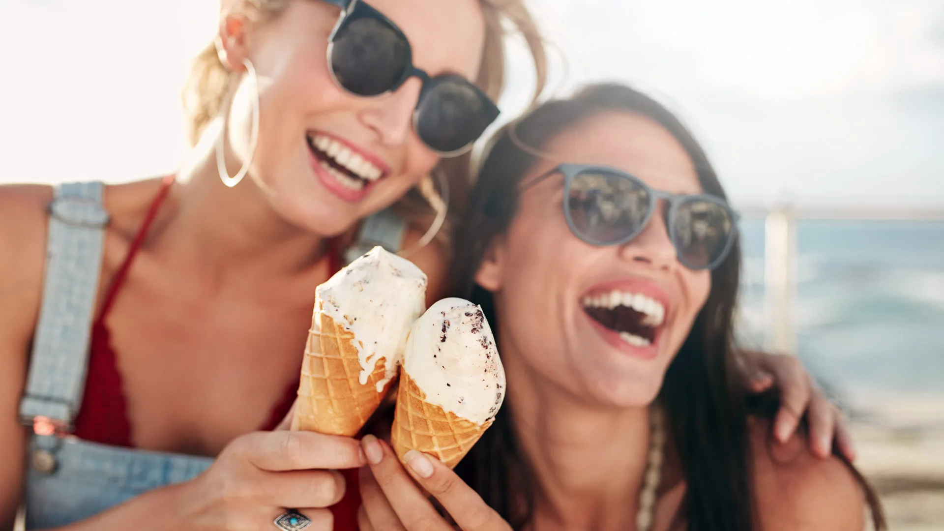 A photograph of two women in sunglasses laughing as they hold two vanilla icecreams