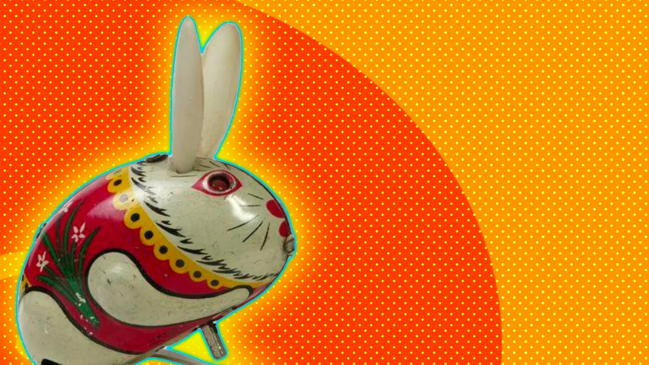 Image of a clockwork tin bunny toy from the V&A collection against an orange dotted background with a yellow halo