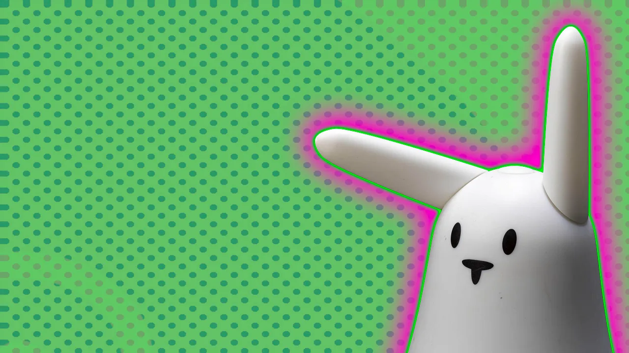 Photograph of a white smart rabbit object with a simple face of black nose and eyes against a green dotted background with a pink halo